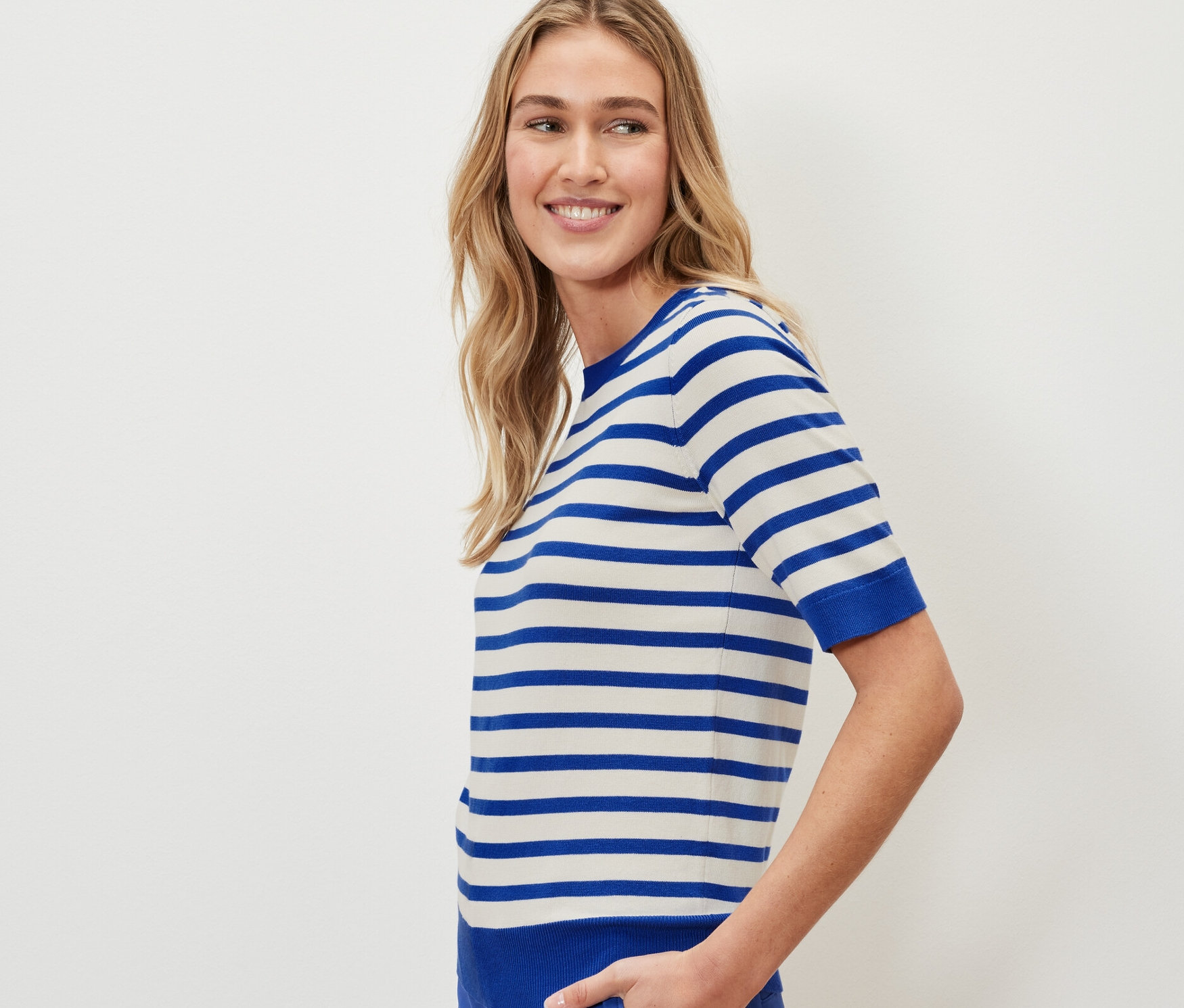 Žena má na sobě proužkovaný svetr z jemného úpletu a modré kalhoty.