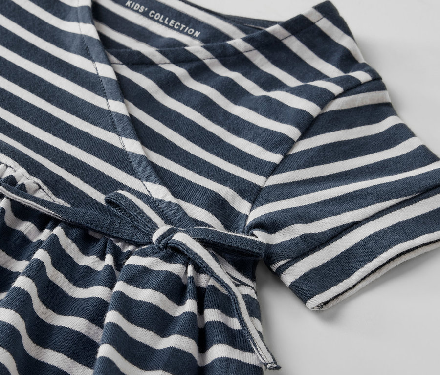 Detail dívčích žerzejových šatů s modrými a bílými pruhy a zavazováním v pase.