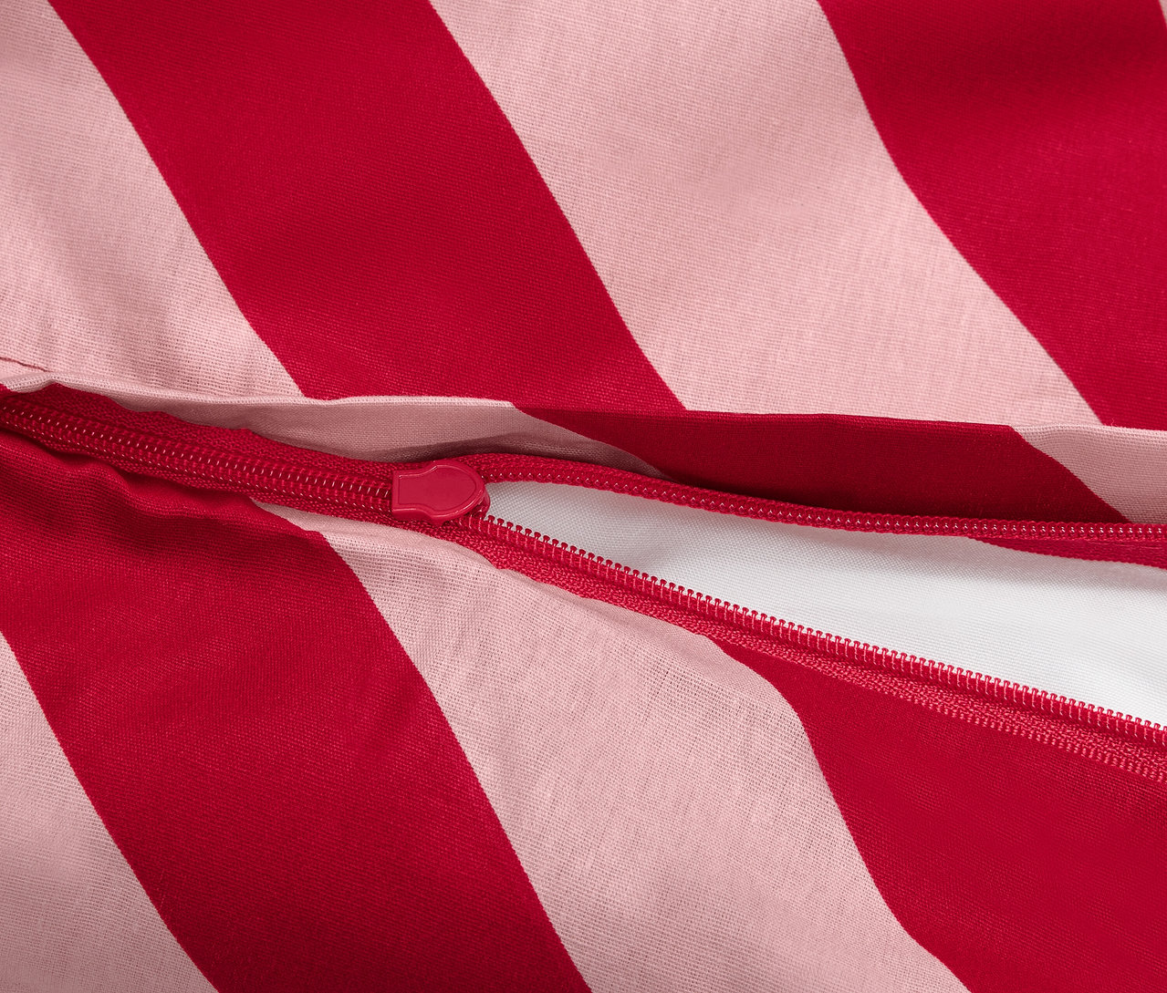 Detail červeno-bílého pruhovaného povlečení se zipem.