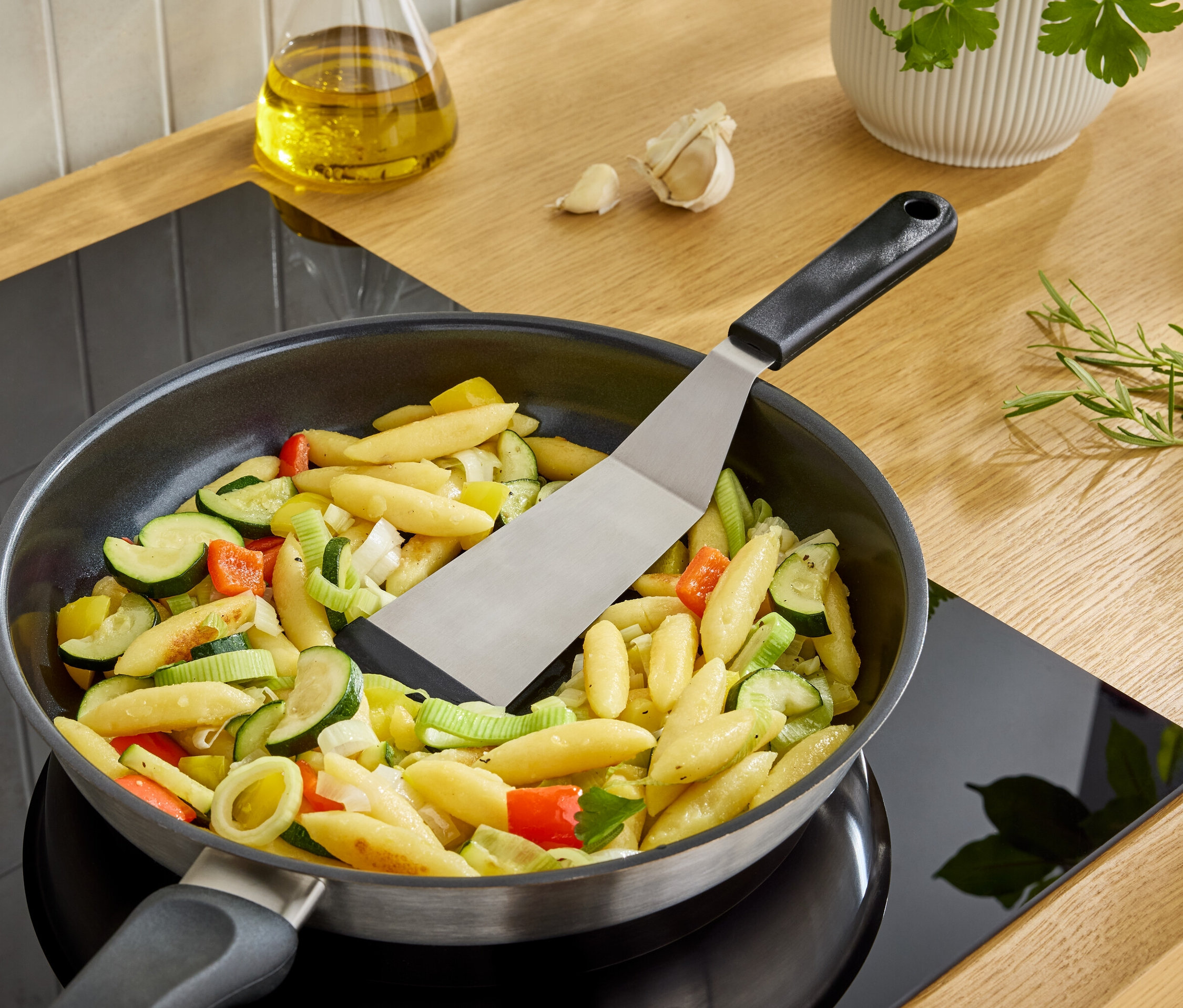 Špachtle obrací noky se zeleninou na pánvi na sporáku.