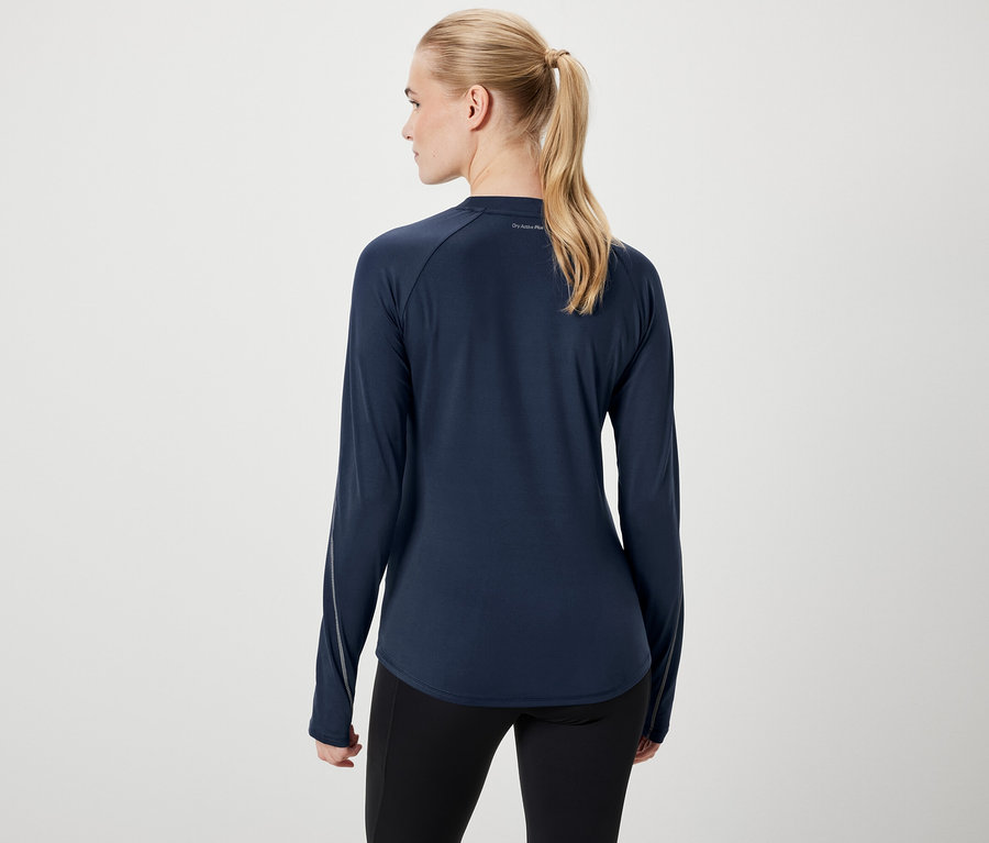 Zezadu je vidět žena s blond vlasy staženými do culíku, oblečená v tmavě modrém tričku s dlouhým rukávem a černých legínách.