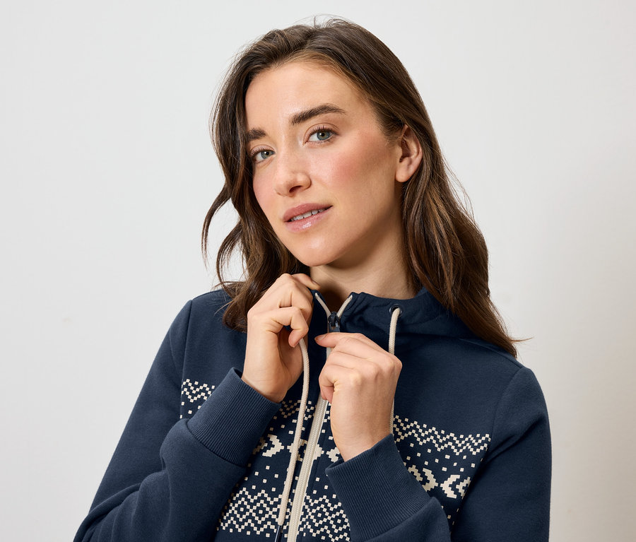Žena si zapíná modrou mikinu s kapucí a bílým vzorem.