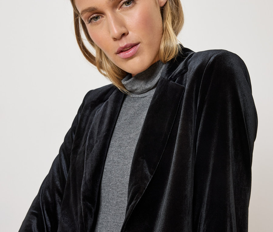 Žena má na sobě černý sametový blejzr a šedý rolák.