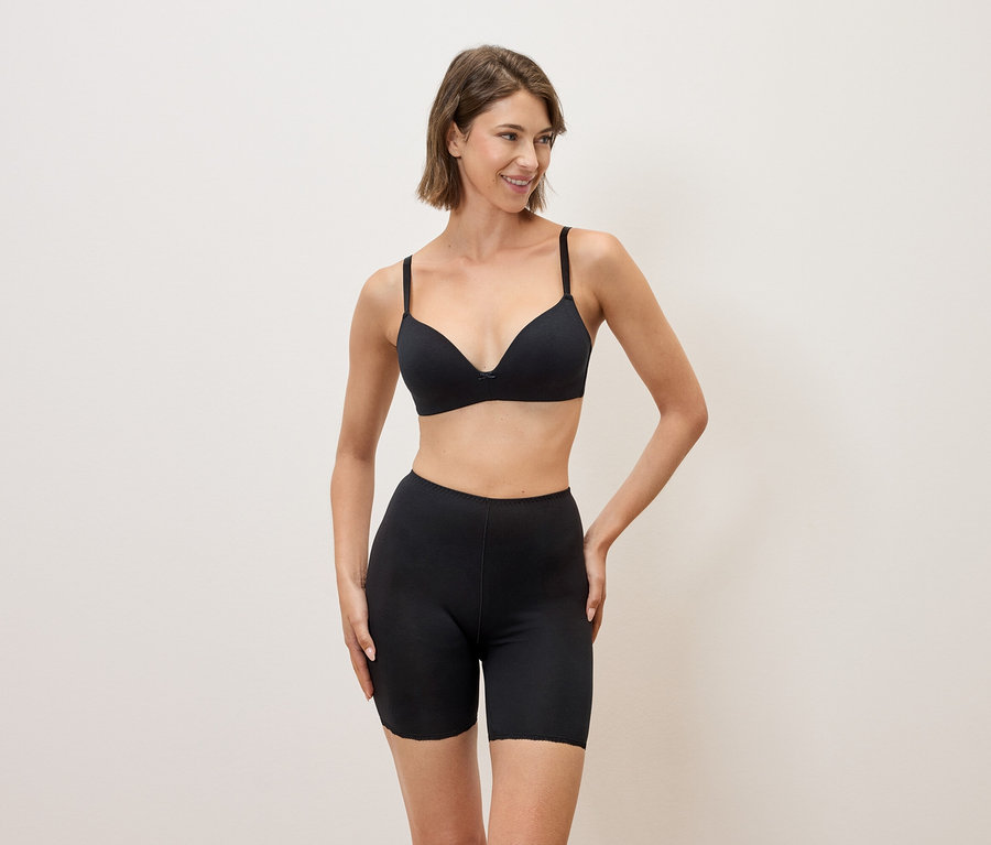 Žena v černé podprsence a černých šortkách pózuje na neutrálním pozadí.