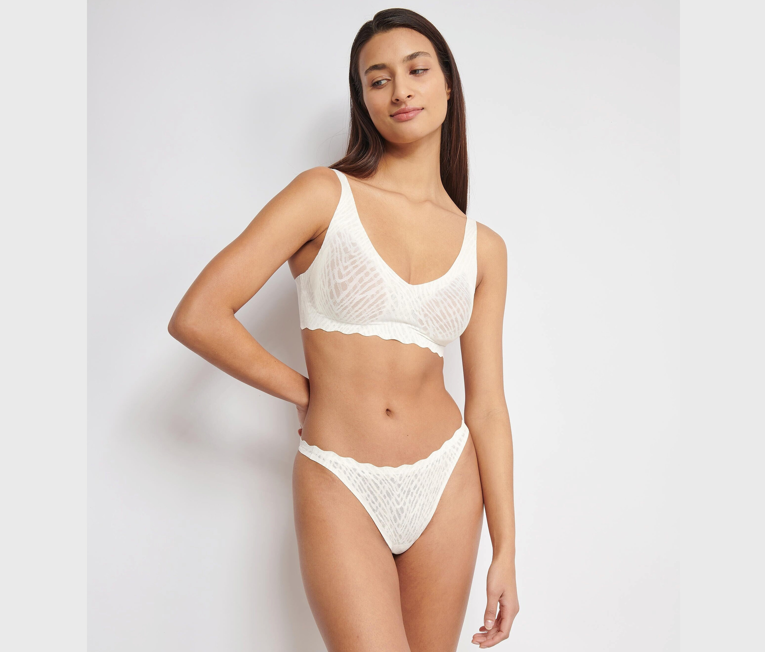 Žena pózuje v bílé soupravě spodního prádla sloggi ZERO Feel Bliss Soft Bra.