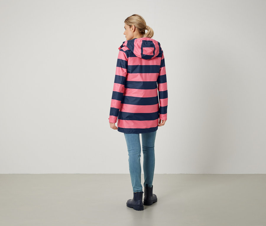 Žena zády k fotoaparátu má na sobě růžovo-modrý pruhovaný kabát, džíny a holínky.