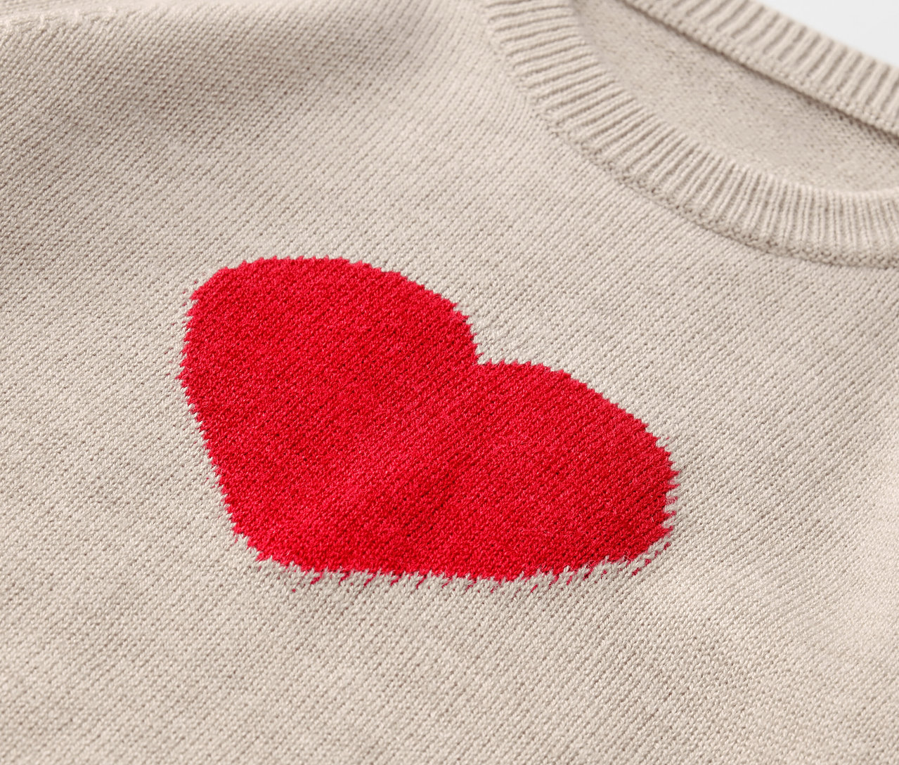 Detail béžového svetru s červeným srdcem.