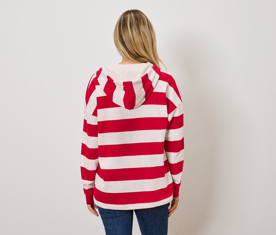 Žena zády k fotoaparátu má na sobě červenobílou pruhovanou mikinu s kapucí a modré džíny.