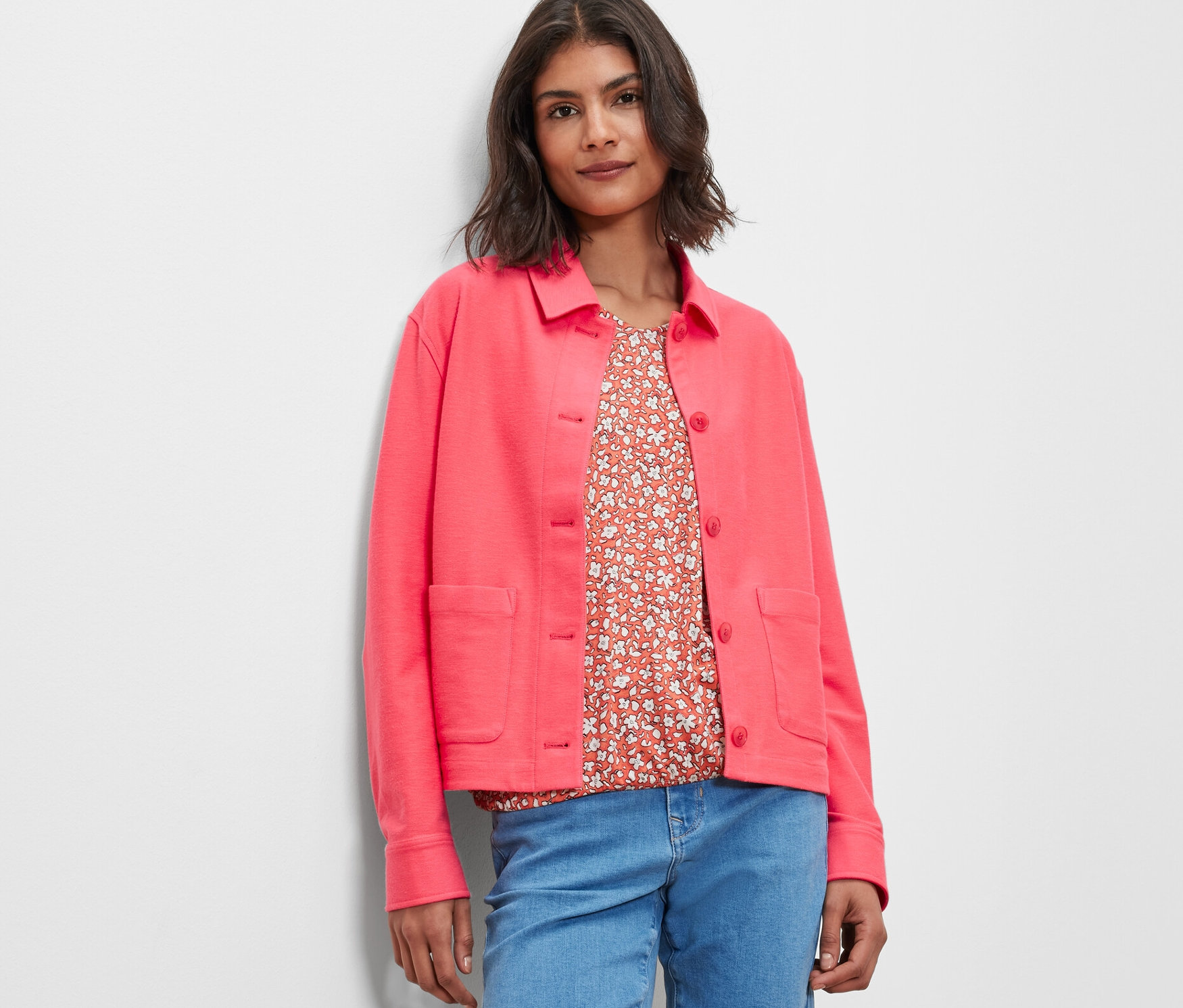 Žena má na sobě růžovou žerzejovou bundu a džíny.