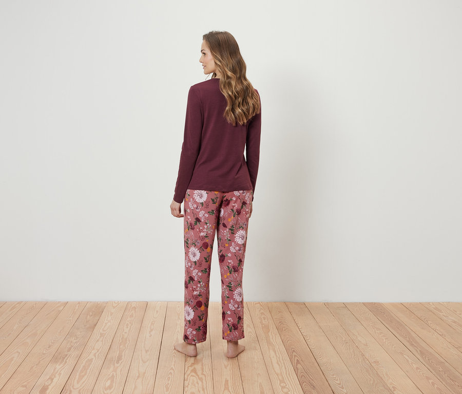 Žena zády k fotoaparátu má na sobě bordó tričko s dlouhým rukávem a růžové květinové pyžamové kalhoty.