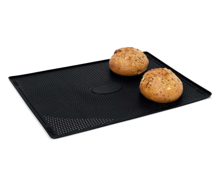 Dva bochníky chleba leží na černé perforované podložce na pečení.
