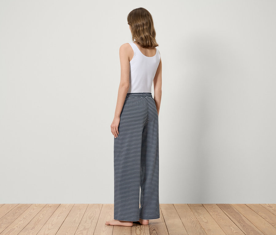 Žena stojí zády, má na sobě bílý top a modré pruhované kalhoty.