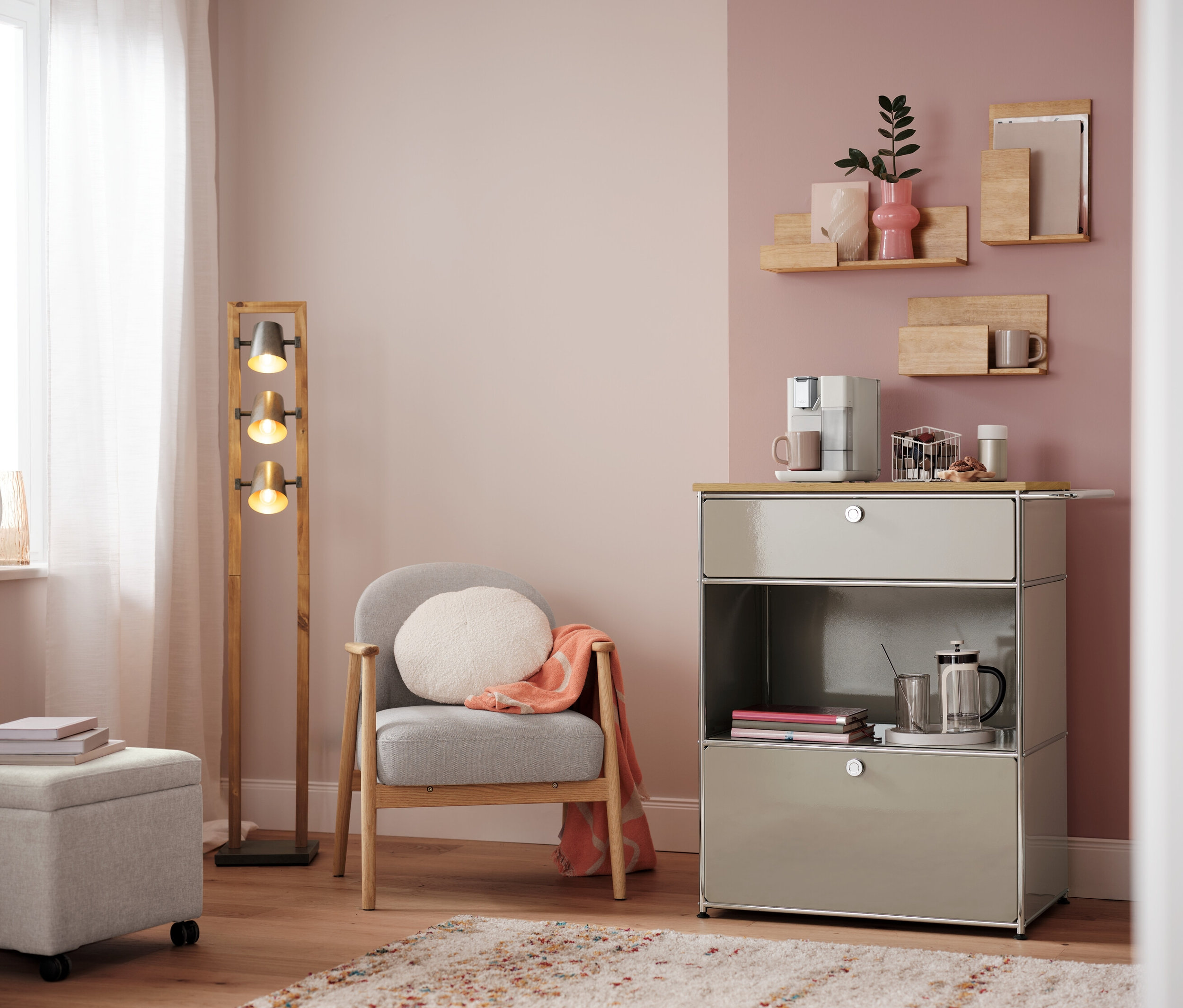 Obývací pokoj s křeslem, lampou a komodou s kávovarem. Na komodě je bílý kapslový koš.