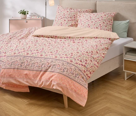 Postel s růžovým květinovým ložním prádlem a odpovídajícími polštáři na dřevěné podlaze.