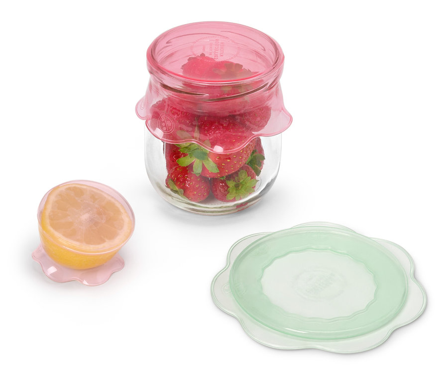 Sklenice s jahodami pod růžovým víčkem stojí vedle půlky citronu pod růžovým víčkem a zeleného víčka.