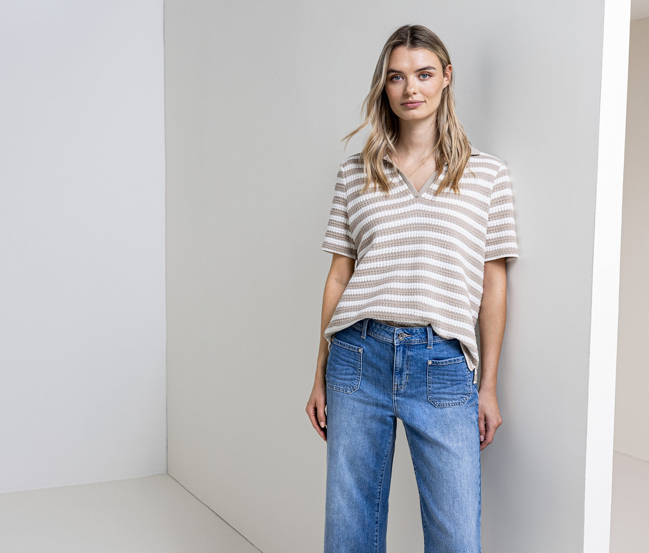 Žena pózuje v džínách a pruhovaném úpletovém tričku Street One před zdí.