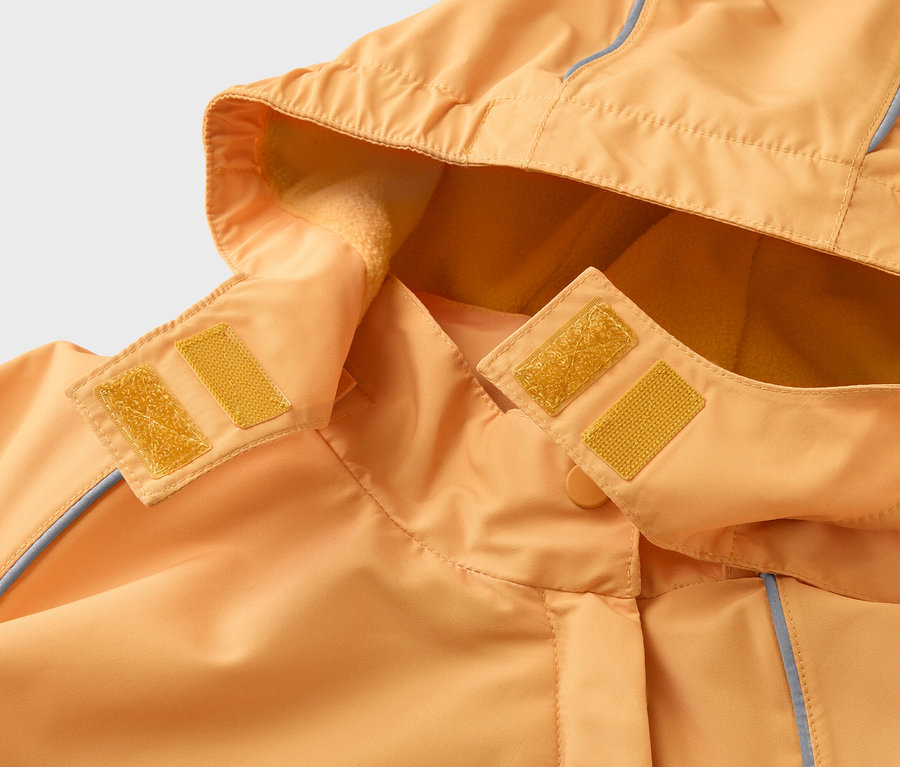 Detail oranžové bundy s kapucí, která se zapíná na žluté suché zipy. Kapuce je podšitá fleecem.