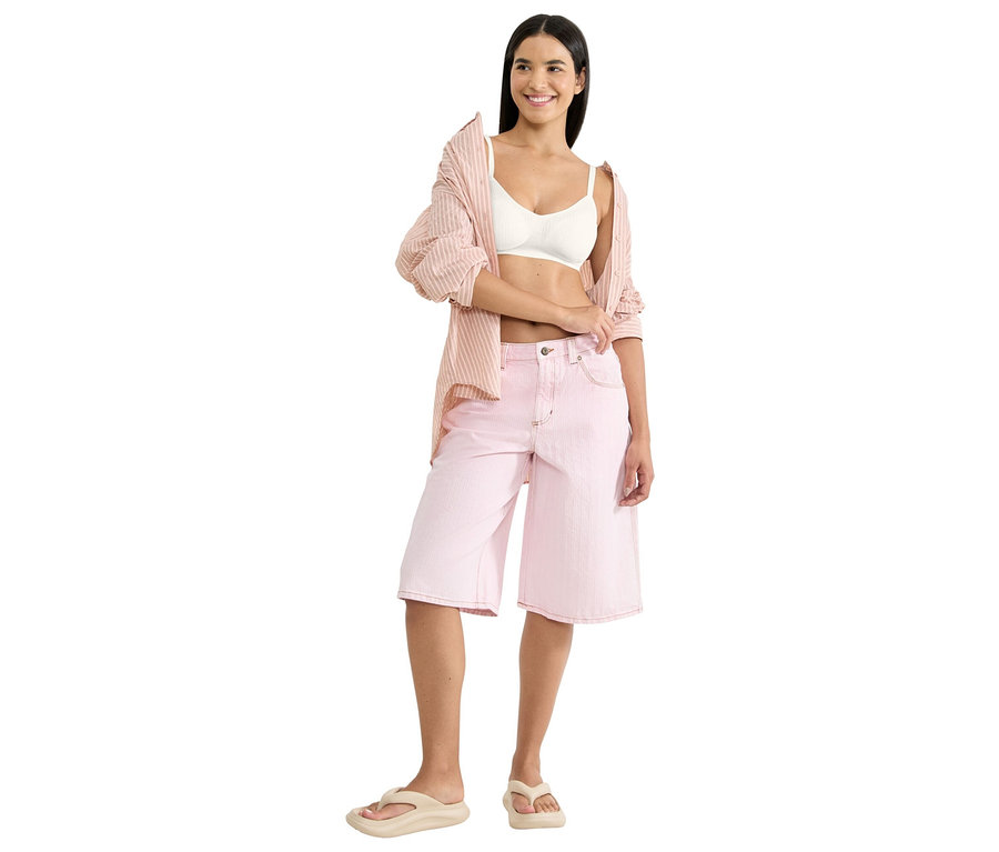 Žena má na sobě bílou braletku, růžovou proužkovanou košili a růžové culottes šortky s béžovými žabkami.