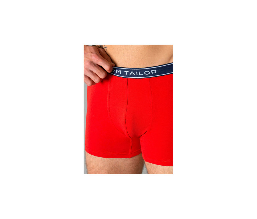 Muž má na sobě červené boxerky Tom Tailor „Buffer“; ruka táhne tmavě modrý pas nahoru.