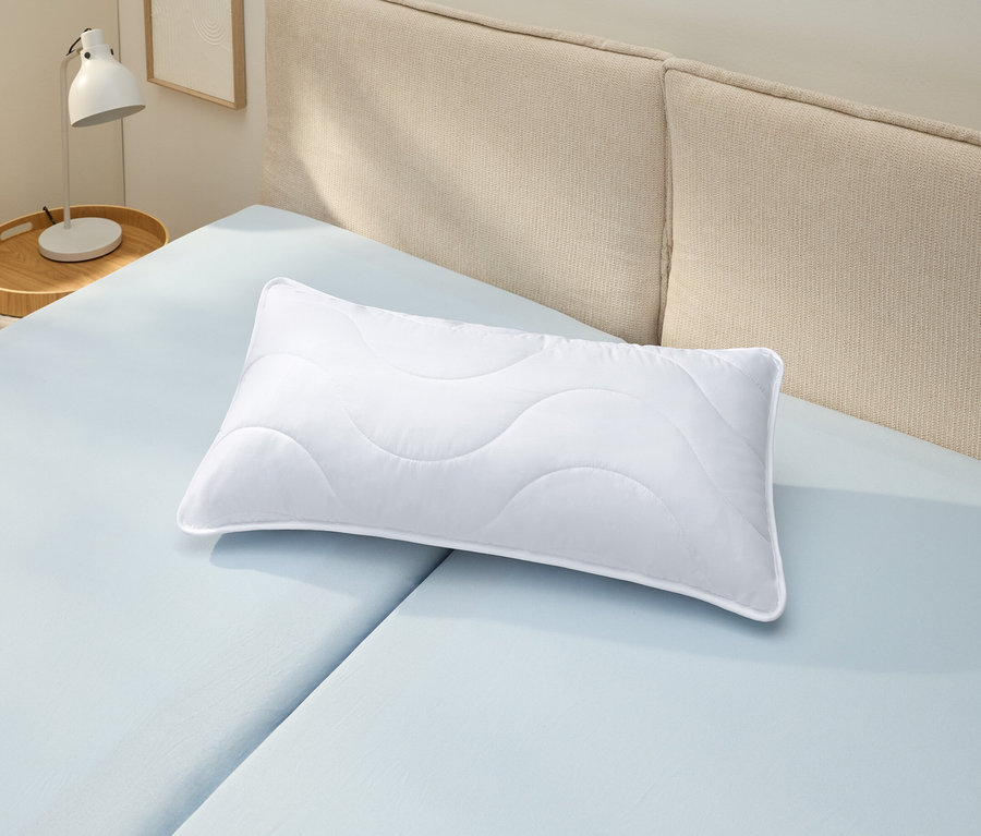Bílý polštář odolný proti varu (cca 80 x 40) leží na světle modrém prostěradle.
