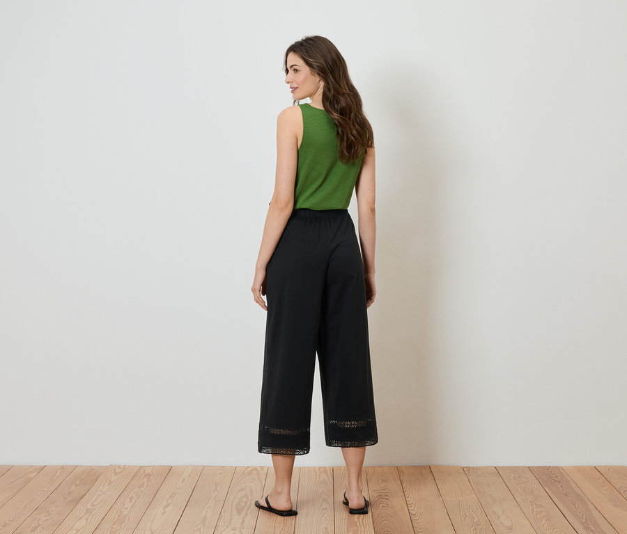 Žena stojí zády k fotoaparátu, má na sobě zelený top a černé culottes s krajkou na spodní straně.