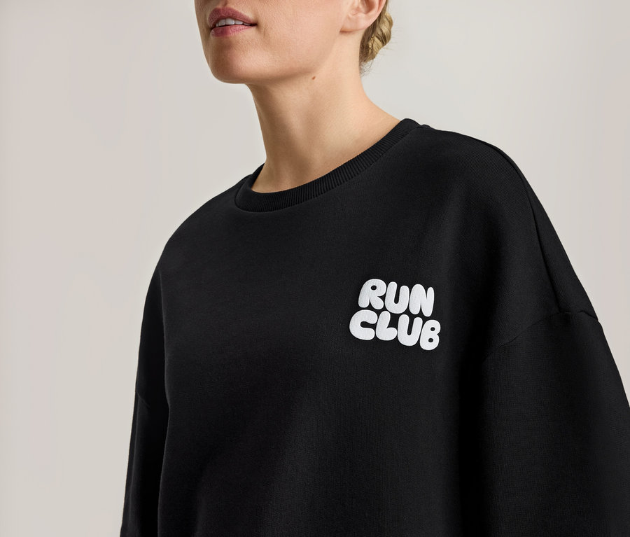 Žena má na sobě černou mikinu s bílým nápisem "RUN CLUB".
