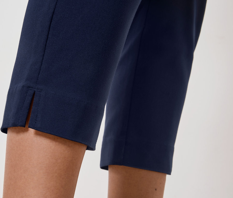 Detailní záběr na nohy osoby, která má na sobě tmavě modré kalhoty s rozparkem na lemu.