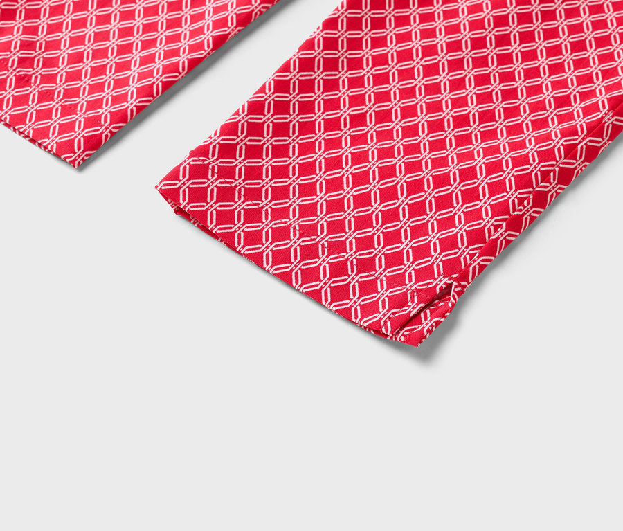 Detailní pohled na dvě červené nohavice s bílým geometrickým vzorem.