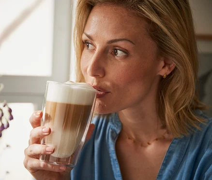 Žena pije latte macchiato ze dvoustěnné sklenice.