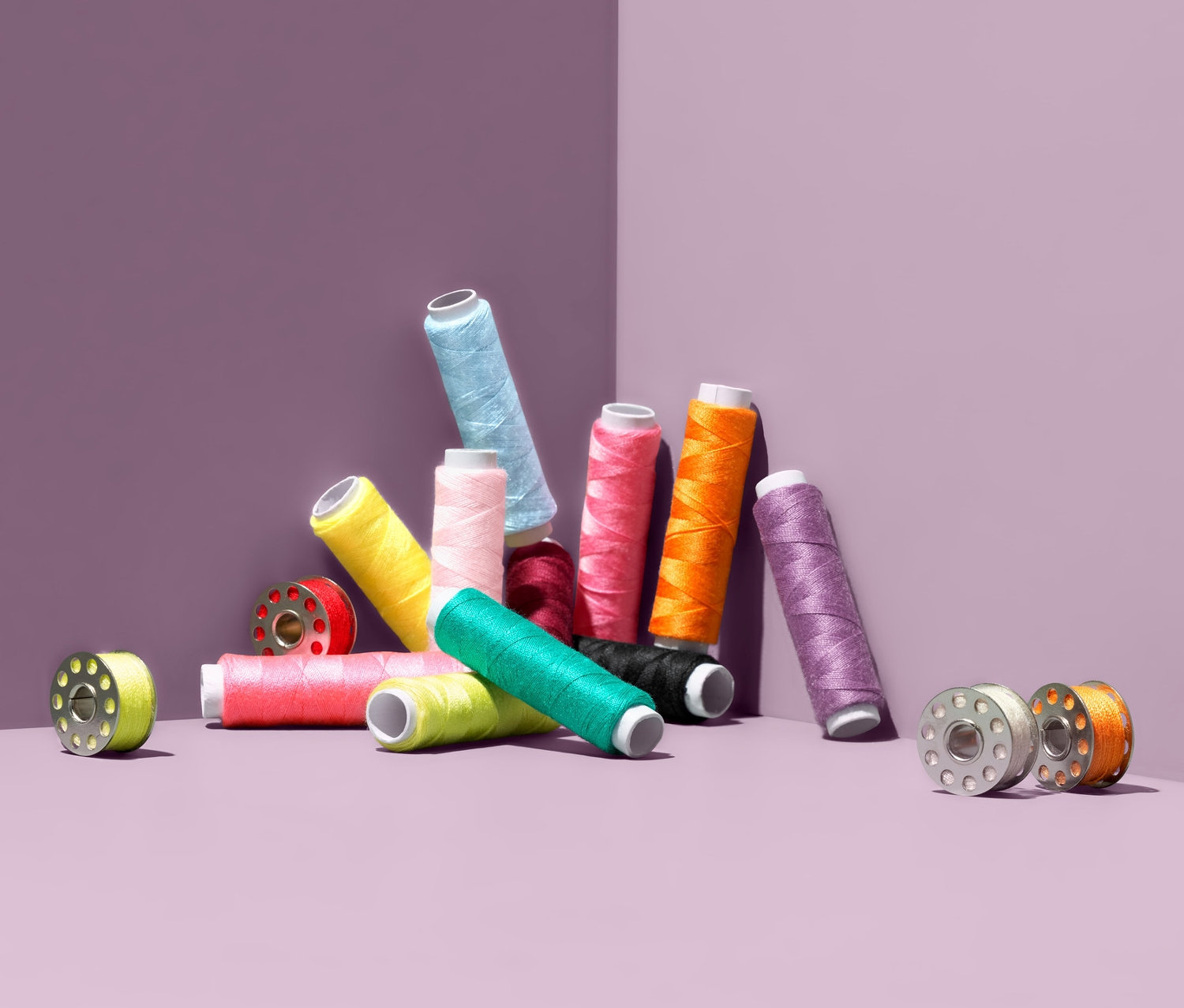 Sada šicích nití různých barev a cívek na fialovém pozadí.