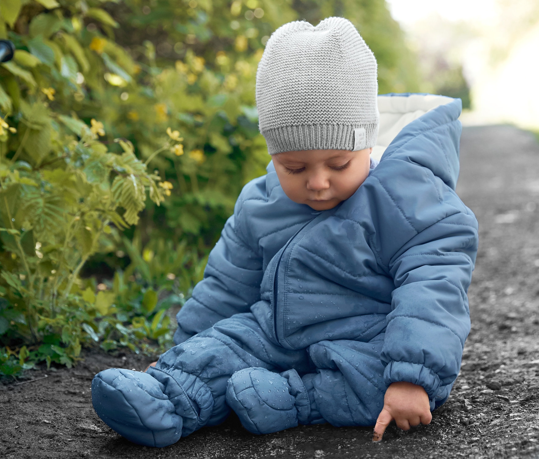 Dítě sedí na zemi v modrém zimním overalu a pletené čepici.