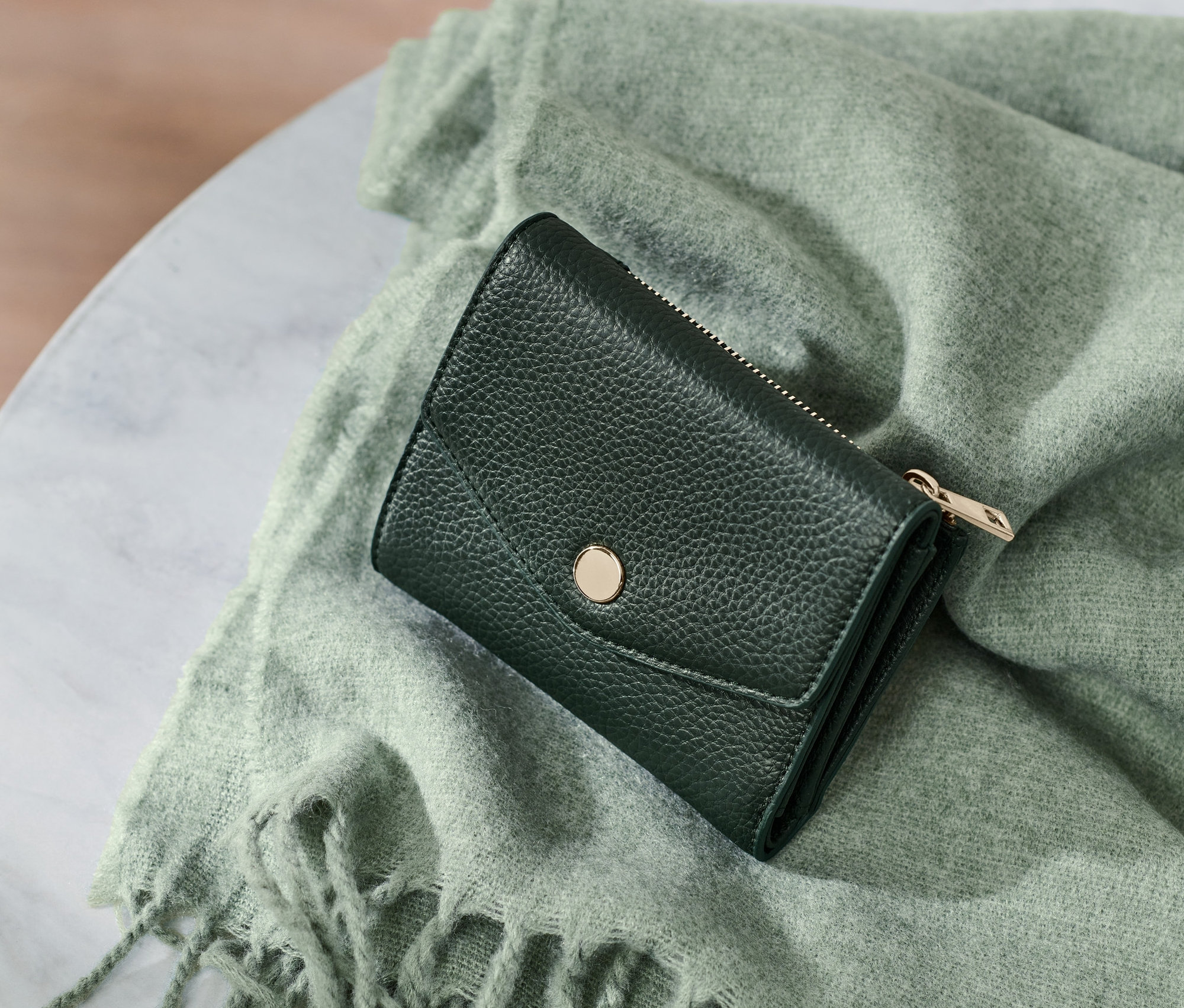 Malá peněženka leží na zeleném šátku s třásněmi na mramorovém stole.