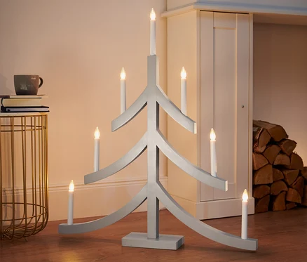 Šedý XL svícen s LED ve tvaru vánočního stromku stojí na podlaze.
