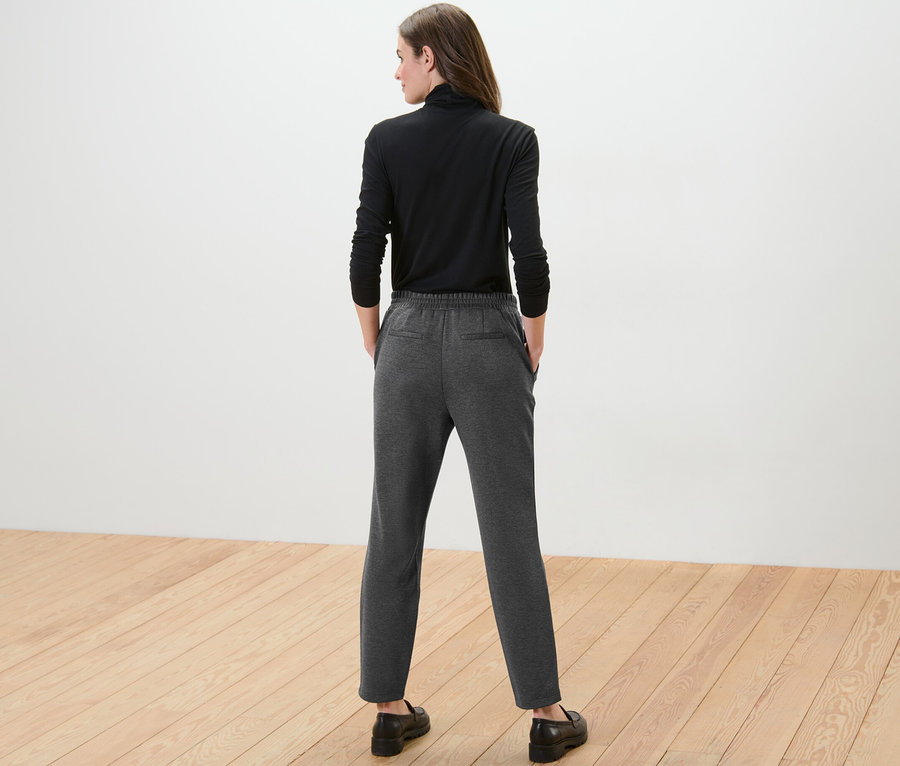 Žena zády k fotoaparátu má na sobě černé tričko s dlouhým rukávem a šedé joggpant kalhoty.