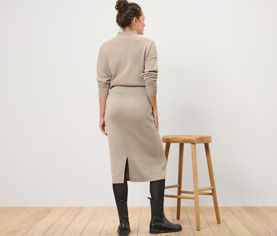 Žena stojí zády a má na sobě pletenou sukni, punčochy a boty.