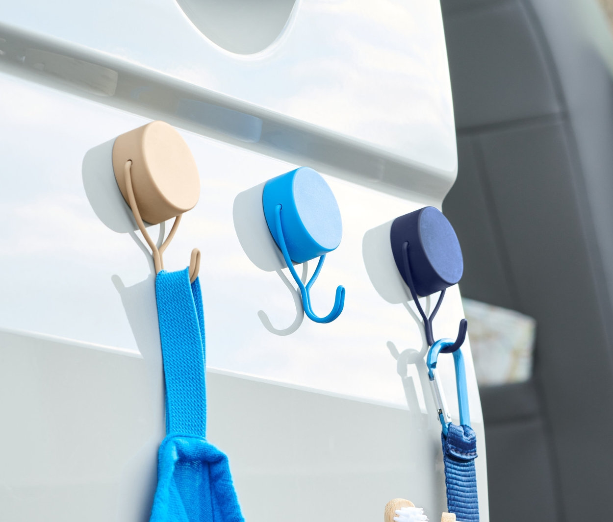 Na bílých dveřích auta jsou připevněny tři magnetické háčky, 3 ks, na kterých visí modrý ručník a toaletní taška.