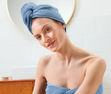Žena sedí zabalená v ručníku a na hlavě má ručníkový turban.