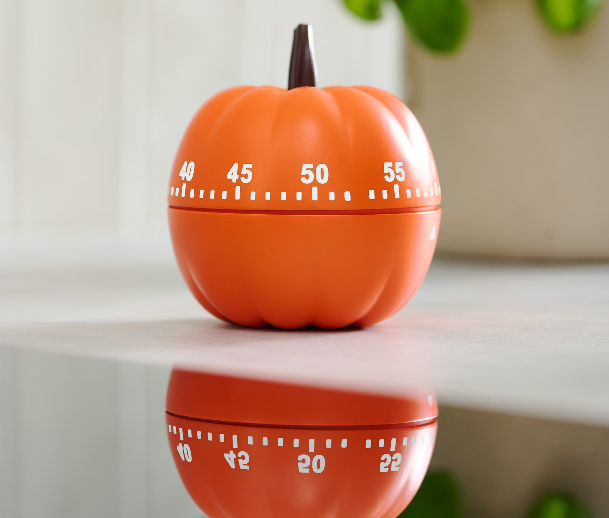 Oranžová minutka ve tvaru dýně na lesklém povrchu.