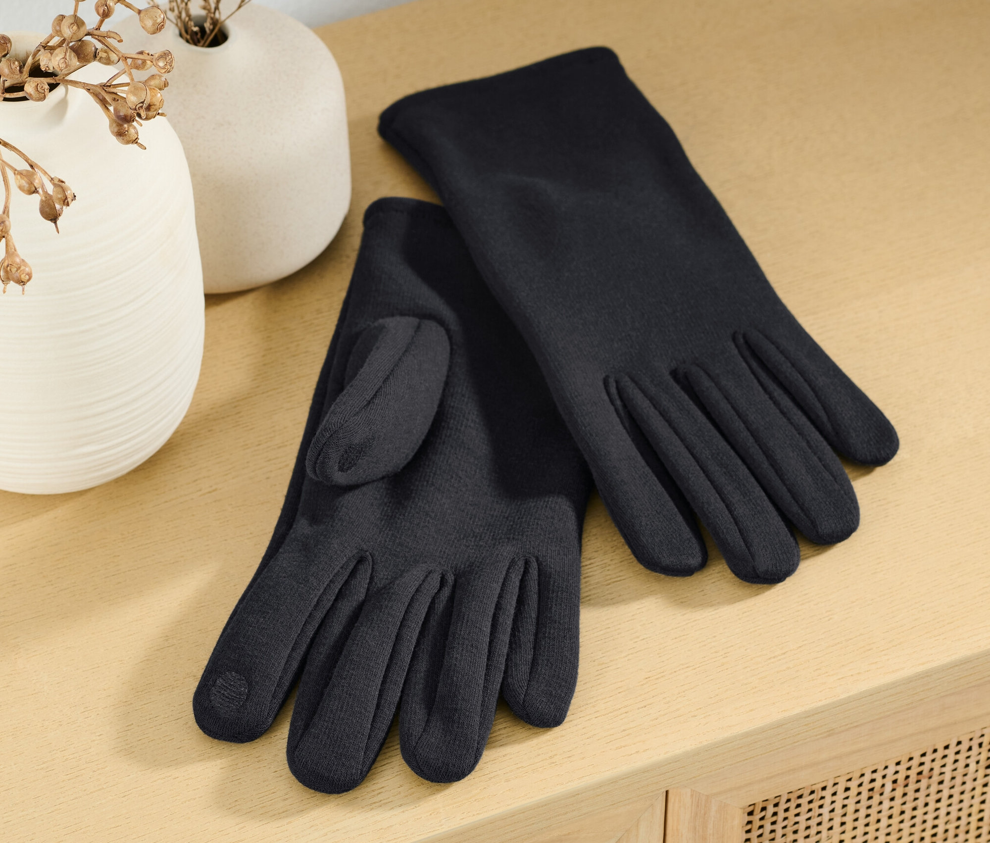 Na stole leží pár rukavic z teplákoviny vedle dvou váz.