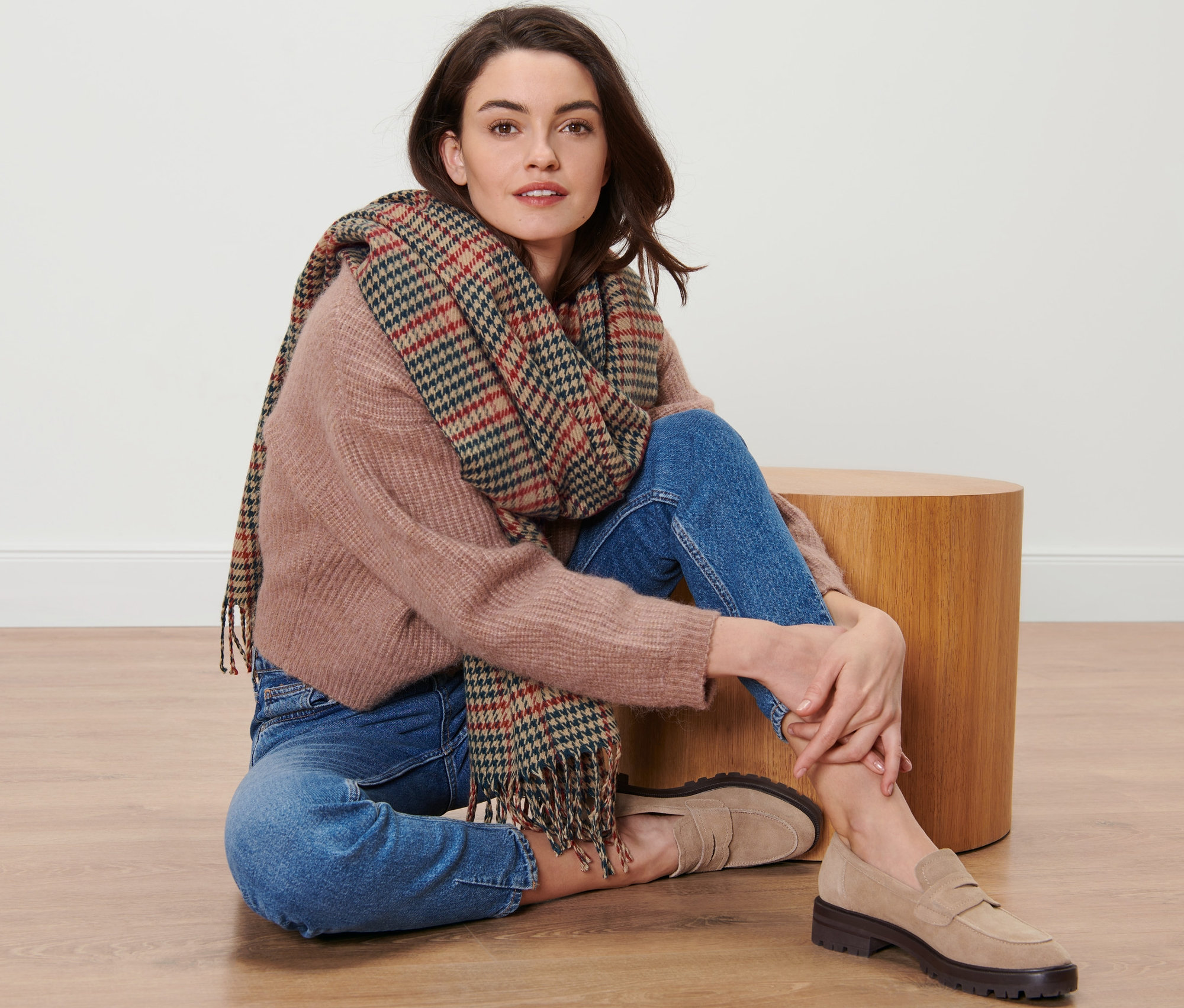 Žena sedí na podlaze a má na sobě kostkovanou tkanou šálu.