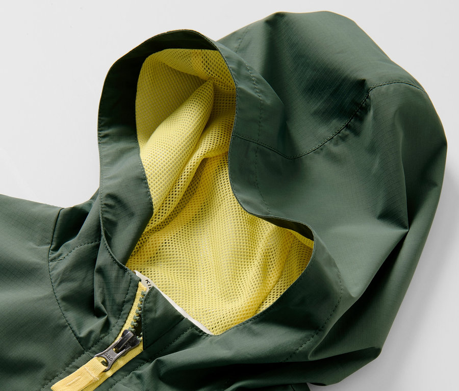 Detail zelené dětské sportovní funkční bundy s kapucí a žlutým zipem.