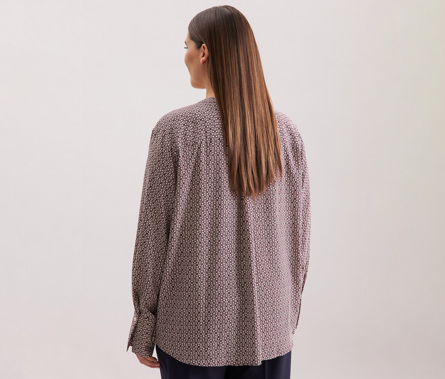 Pohled zezadu na ženu s dlouhými hnědými vlasy, oblečenou v tunice z viskózy Seidensticker s celoplošným potiskem v ecru a burgundské barvě.