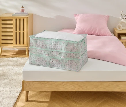 Na posteli leží velký úložný box s květinovým vzorem.