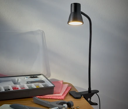Černá LED lampa s klipem stojí na stole vedle sady na šití.