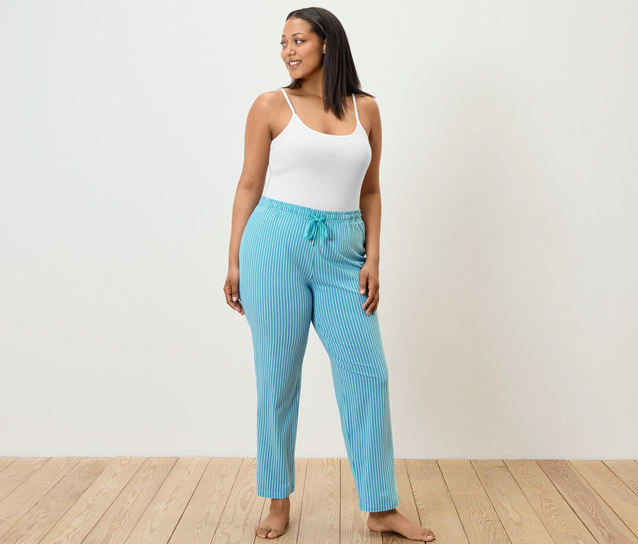 Žena stojí a má na sobě pyžamové kalhoty a tílko.