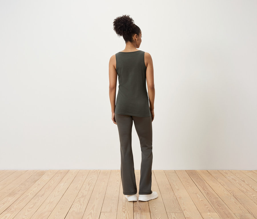 Žena stojí zády, má na sobě tílko a kalhoty.