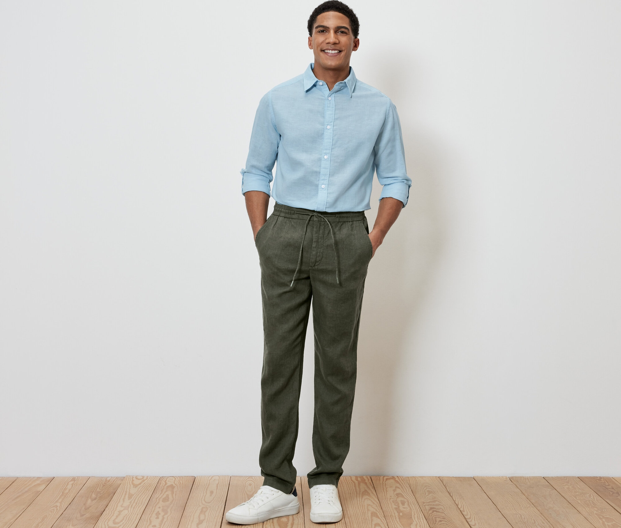Muž stojí a má ruce v kapsách lněných kalhot chino khaki.