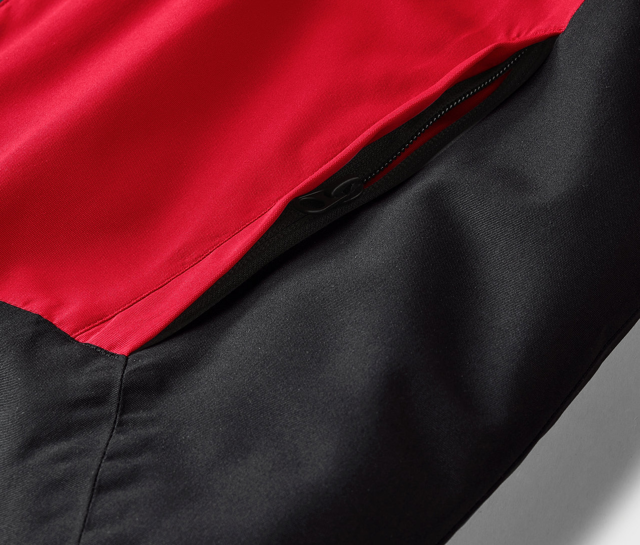 Detail červeno-černé bundy se zipem na kapse.