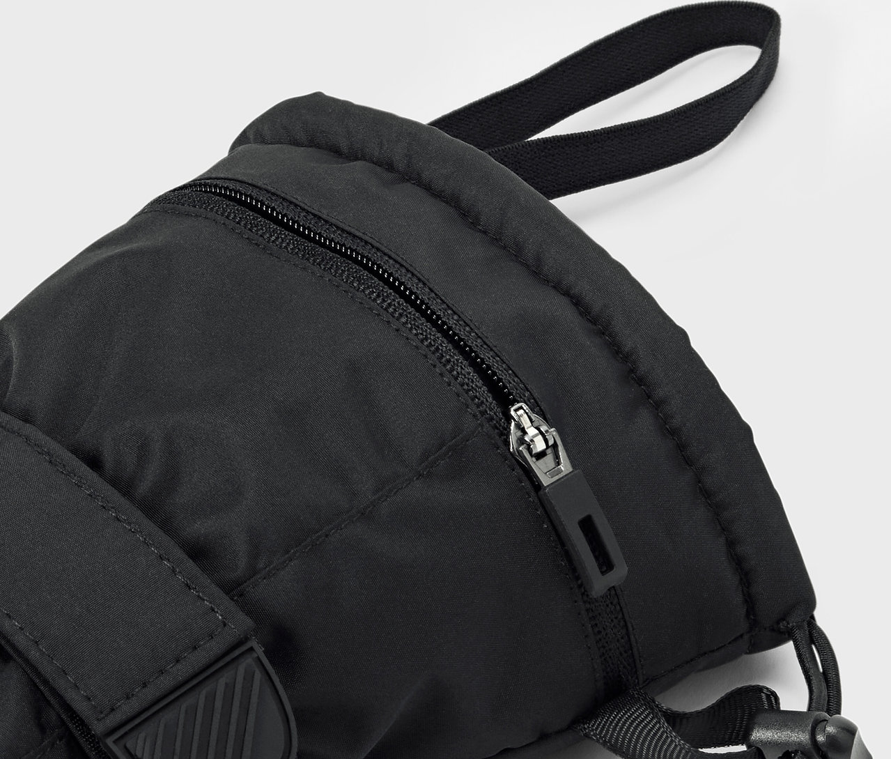Detail černého batohu s viditelným zipem a popruhem.