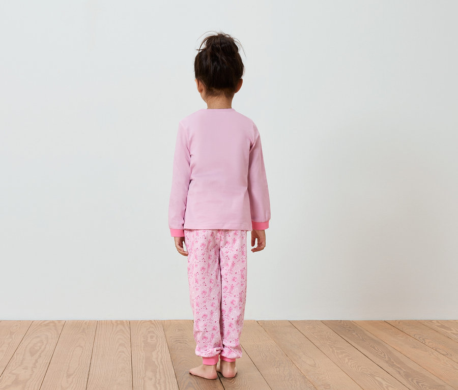 Dívka v růžovém pyžamu stojí zády k fotoaparátu.